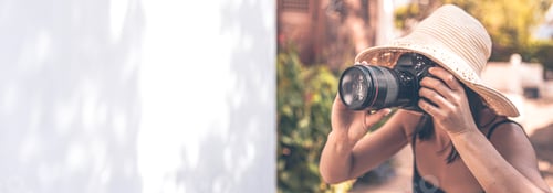 Preview: A woman in a hat takes pictures with a professional SLR camera on a summer day.