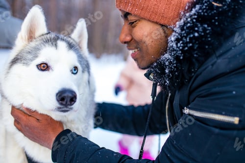 Preview: mixed race man hug his dog husky in winter forest park close up
