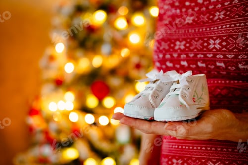 Preview: Tiny Shoes Held in Front of Christmas Tree