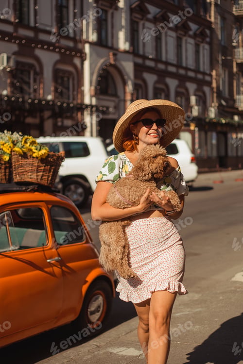 Preview: A young beautiful woman in sunglasses walks around the city on a summer day holding her puppy in he