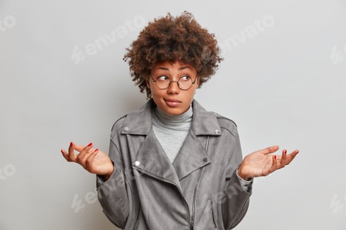 Preview: Confused hesitant young woman spreads palms has doubtful face expression stands uncertain shrugs sho