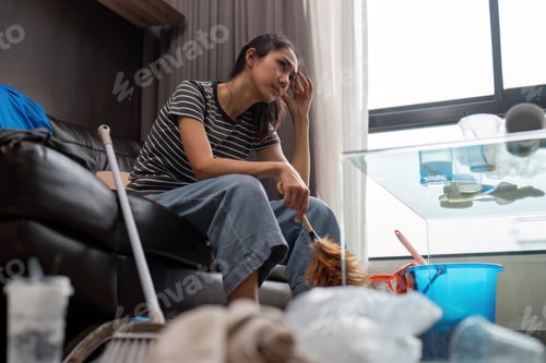 Preview: Tired young woman asian in the living room with cleaning products and equipment, housekeeper or