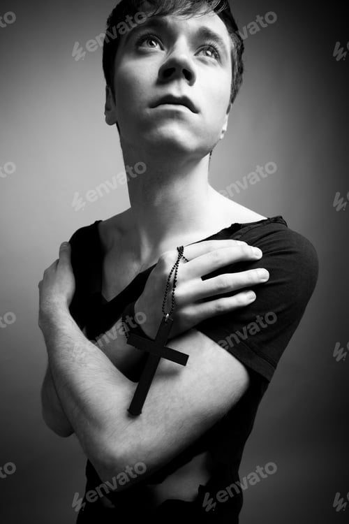 Preview: Young man in modern black clothing holding big black cross in hands