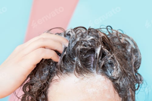Visualização: A woman washes her hair with shampoo on pink and blue background, front view.