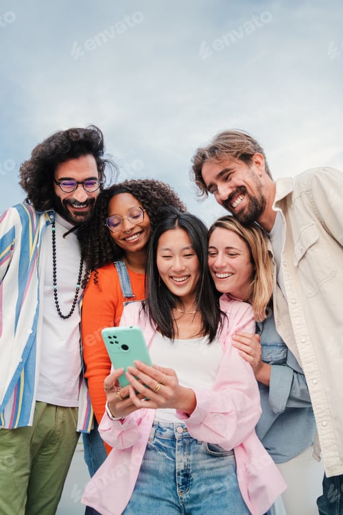 Preview: Vertical portrait of a multiracial group of young adult friends enjoying and smiling using a mobile