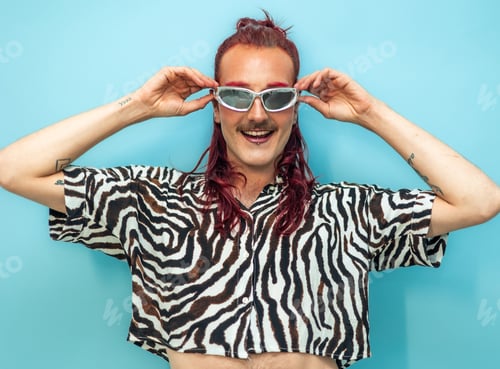 Preview: Non-binary person with pink hair and sunglasses is smiling on blue background