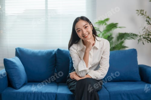 Preview: Young Asian businesswoman smiling while sitting on blue sofa in modern office