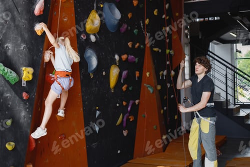 Preview: Kid girl at climbing wall with male instructor in climbing center