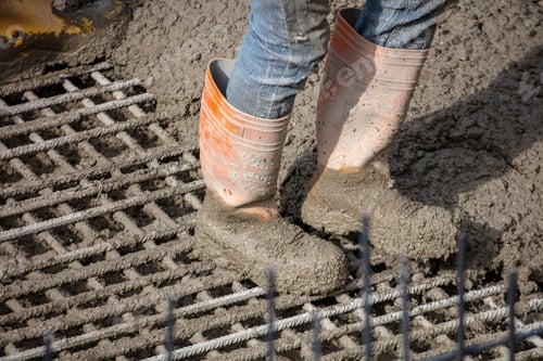 Preview: Construction worker wearing orange boots standing upon wet concrete and steel rebar