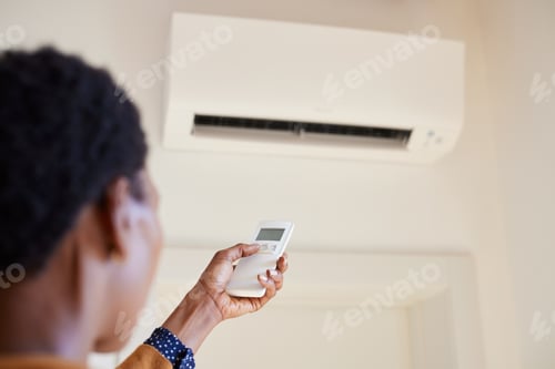 Preview: African american woman holding remote control aimed at air conditioner