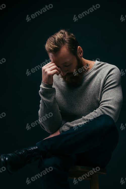Preview: Sad man in grey long sleeve sitting on chair isolated on black