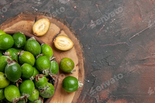 Preview: Half shot of fresh green feijoas in a brown pot on wooden tray on dark background
