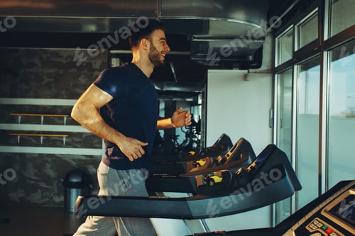 Preview: Young handsome man in sportswear running on treadmill at gym