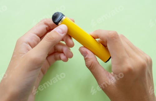 Preview: electronic cigarette in the hands of a teenager on a green background, the danger of electronic ciga