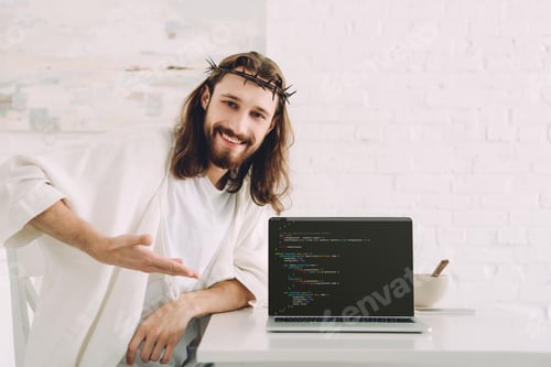 Preview: happy Jesus holding cup of coffee and pointing at laptop with html code in kitchen at home