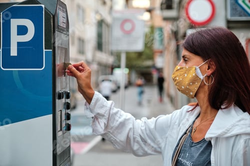 Preview: adult woman with mask insert coins in park meter