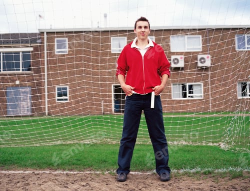 Preview: Confident young man standing in front of a soccer goal on a cloudy day.