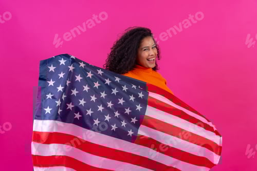 Preview: Curly-haired woman with the usa flag on a pink background, studio shot