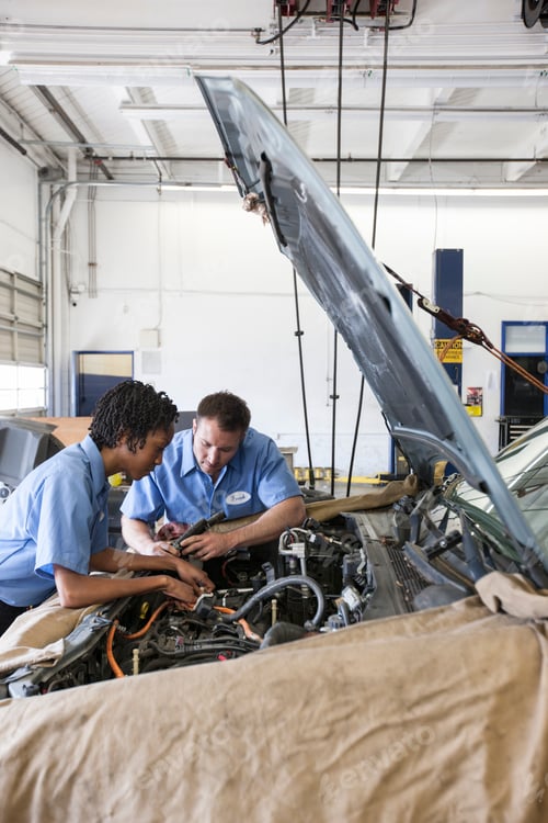Preview: Male and female mechanics talk as they look at engine in auto repair shop