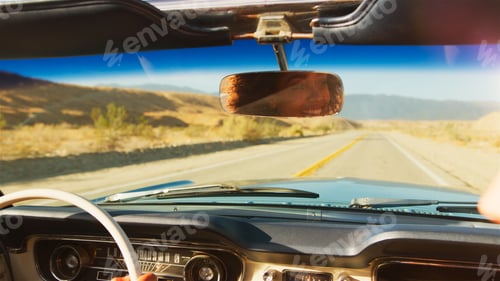 Preview: Female Driver Reflected In Mirror Driving Classic Open Top Car On Road Trip Through Countryside