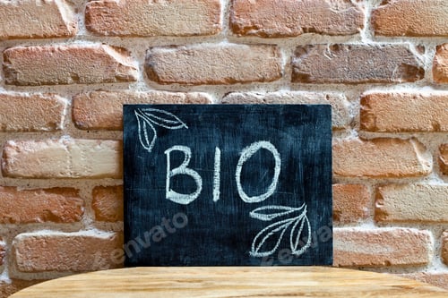 Preview: Chalk board with the word BIO drown by hand and chalks on wooden table on brick wall background.
