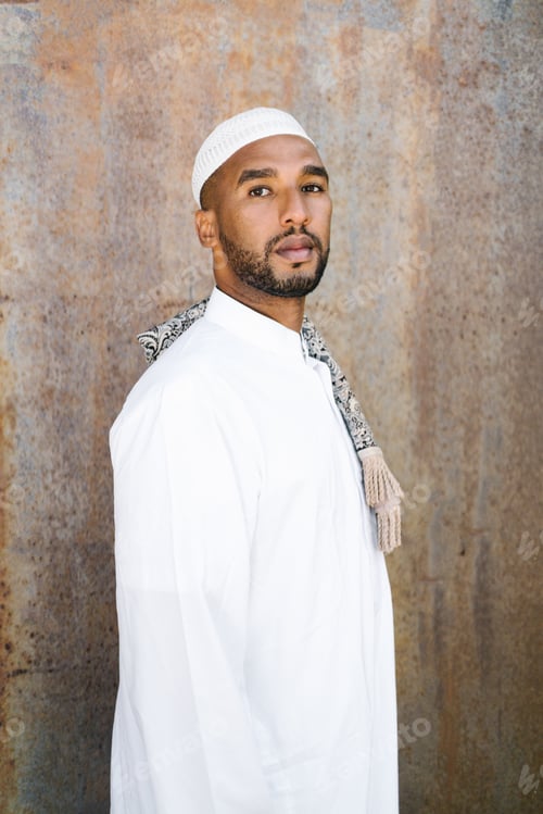 Preview: Islamic male in authentic white clothes looking away while standing against grungy wall