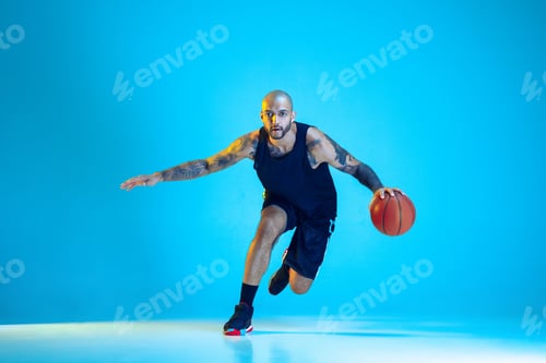 Preview: Young basketball player training isolated on blue studio background in neon light