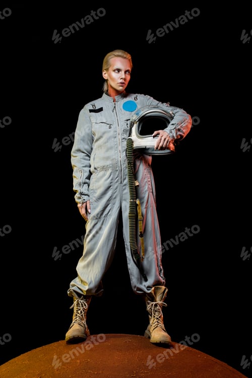 Preview: attractive female cosmonaut in spacesuit holding helmet and standing on planet
