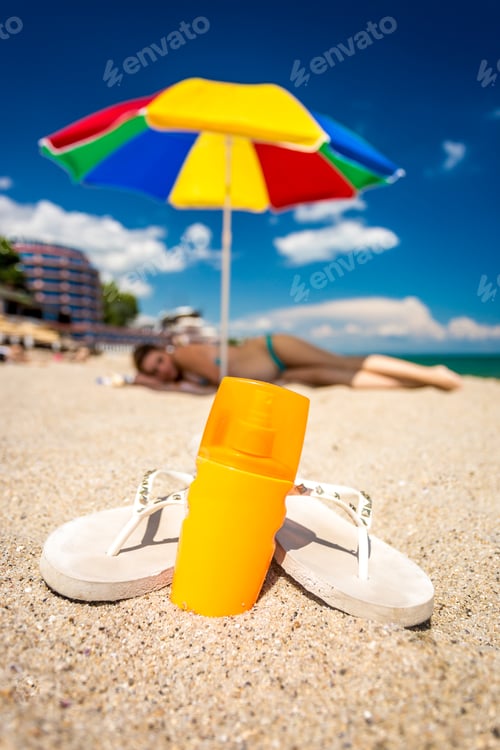 Preview: Closeup shot of flip-flops and sunblock lotion lying on beach