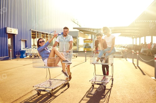 Preview: Group of happy young people having fun on shopping trolleys. Young people racing on shopping cart.