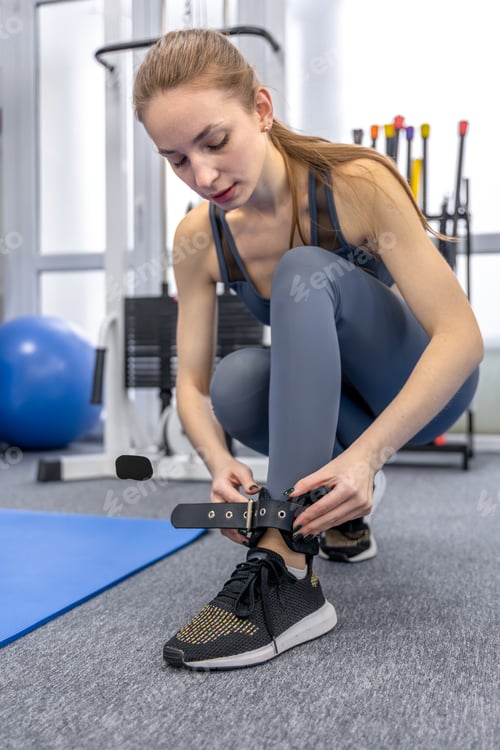 Preview: Female patient fastens ankle strap in rehab gym. Ankle strap.
