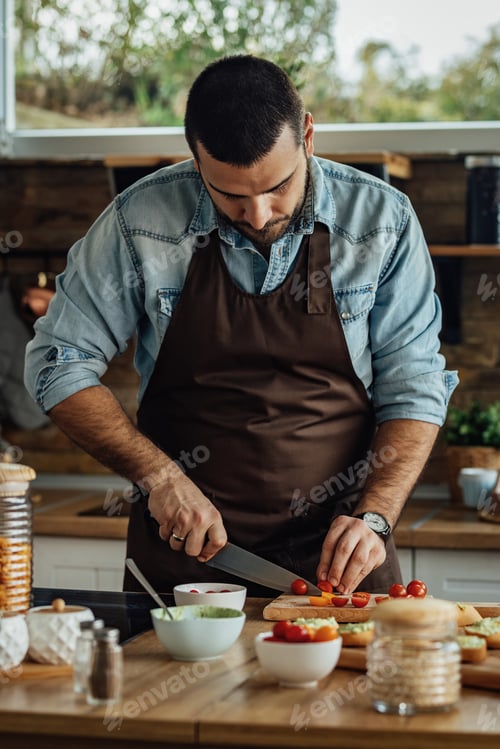 Preview: Young man slicing cherry tomato in the kitchen.