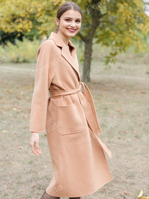 Preview: Woman with brown hair in a long trench coat walking on the park.