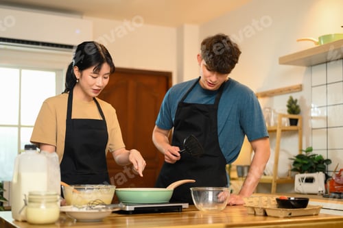 Preview: Happy young couple in aprons preparing to cook pancakes in a cozy home kitchen