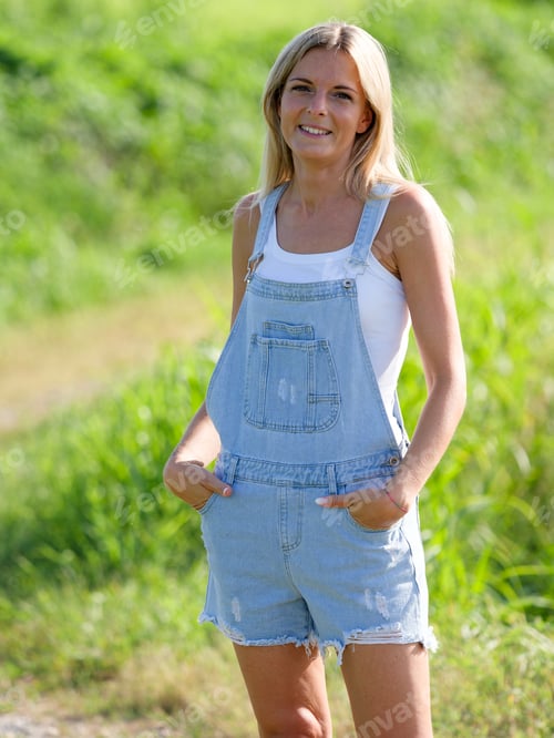 Preview: Woman smiling in a field wearing a denim overall shorts on a sunny day, Italy