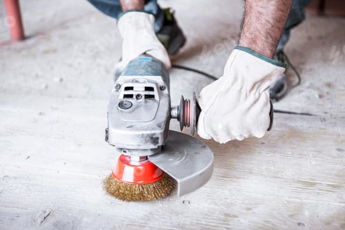 Preview: A worker holds an electric sander with metal bristles in his hands.