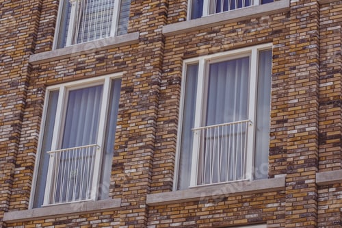 Preview: Low angle shot of a building with colorful bricks with white window and white curtains