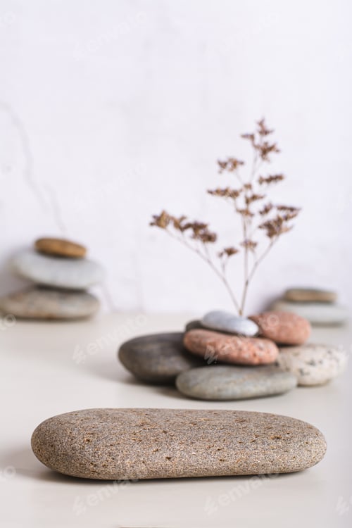Preview: A podium made of smooth sea stone and a dried flower from a pile of stones vertical view