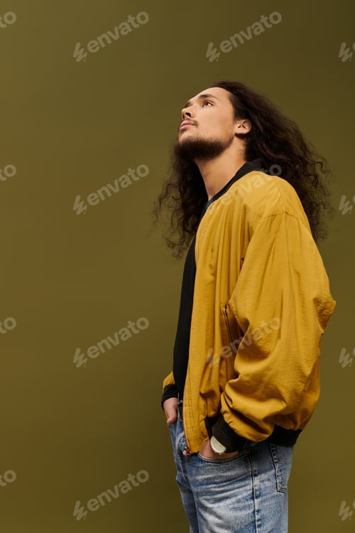 Preview: Young bearded man in stylish jacket gazes thoughtfully at the ceiling in modern studio space