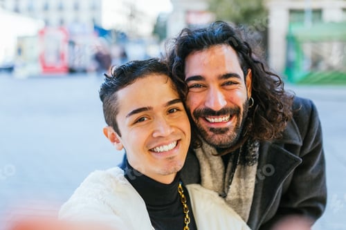 Preview: Happy gay couple smiling while taking selfies together outdoors.