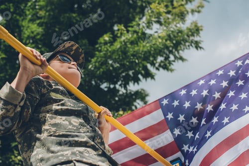 Preview: low angle view of boy in sunglasses pulling himself up on crossbar with american flag on backdrop