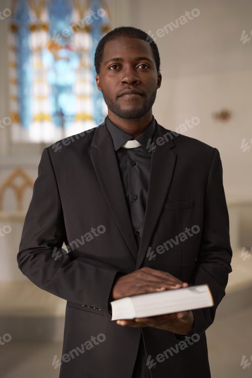 Preview: Black Young Man as Priest Holding Bible Standing at Altar in Church