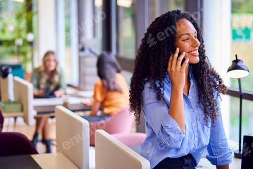 Preview: Businesswoman Standing By Partition In Open Plan Office Making Call On Mobile Phone