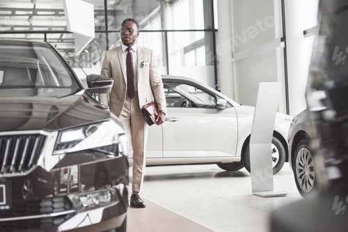 Preview: Young black businessman on auto salon background. Car sale and rent concept