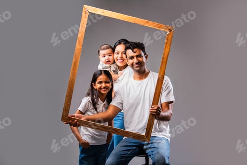 Preview: Looking through photo frame Indian family smiles joyfully sitting together against gray background