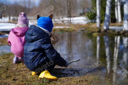 Preview: Colored paper boats,ships.Little girls in pink, purple waterproof rubber boots cheerfully jumps thro