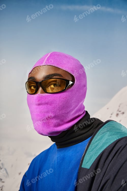 Preview: young african american man in pink balaclava and sunglasses looking at camera, winter concept