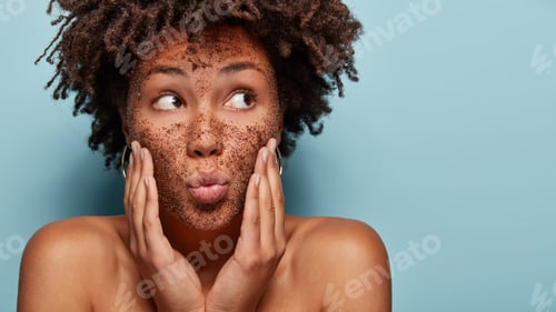 Preview: Curious black lady focused aside has coffe scrub on face applies mask on face, focused aside, has ba