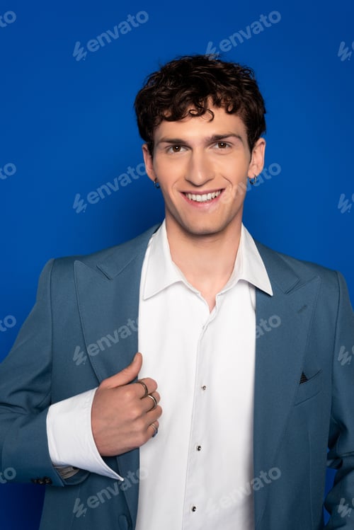 Preview: Portrait of smiling and curly model in blazer looking at camera on blue background