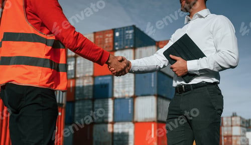 Preview: Making handshake. Two male workers is on the location with containers